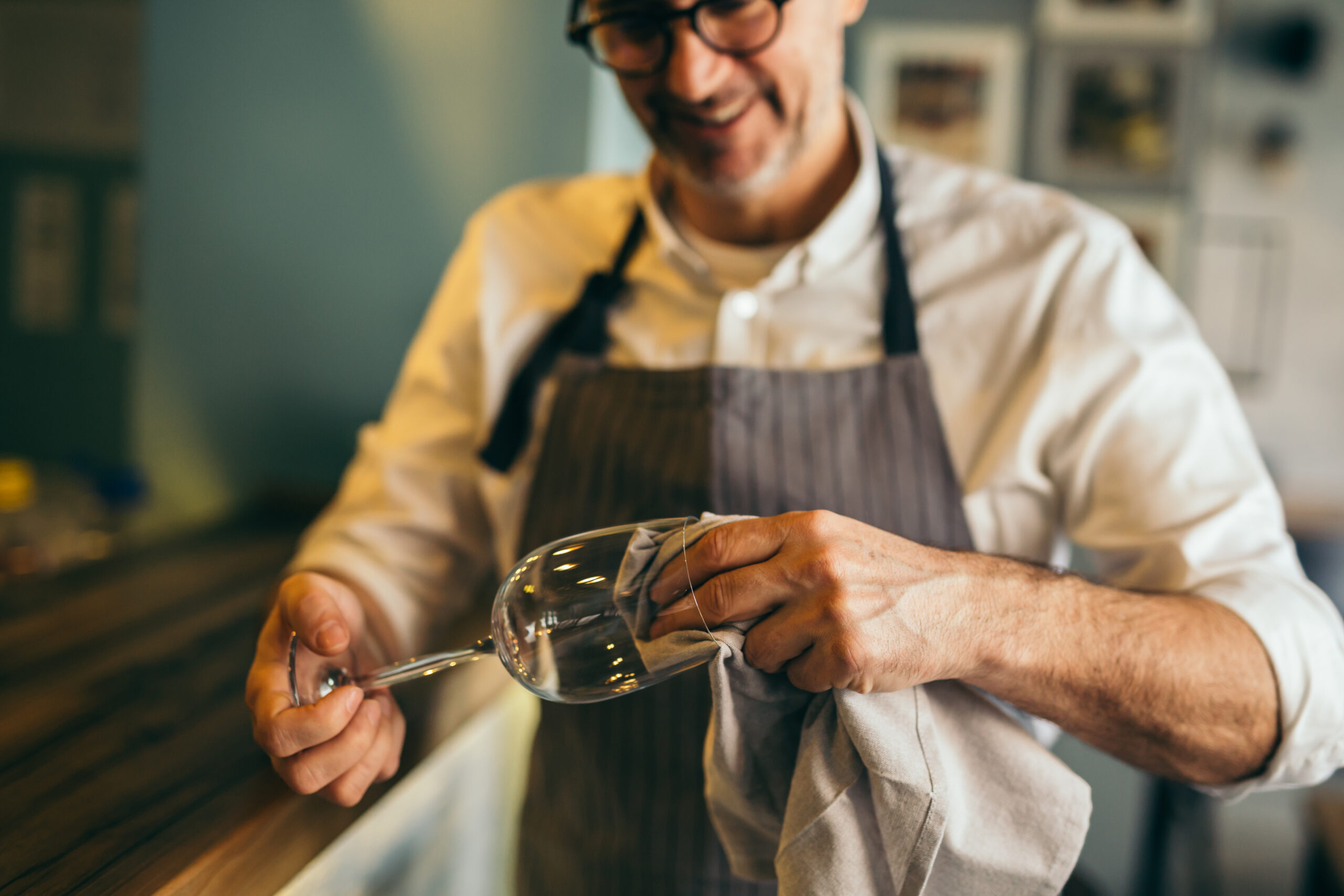 Middle,aged,barman,polishing,the,wine,glass,in,cafe,bar